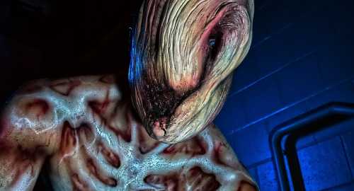 A grotesque, humanoid creature with distorted features and textured skin, illuminated by eerie blue light.