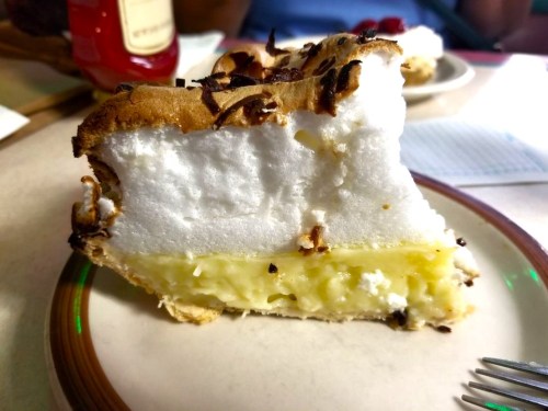 A slice of coconut cream pie with a golden filling and fluffy meringue topping, served on a plate.