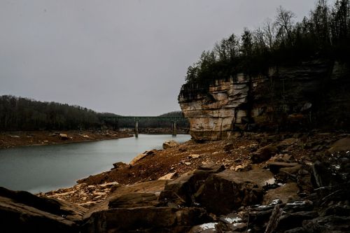 A serene lake surrounded by rocky cliffs and sparse trees under a cloudy sky.