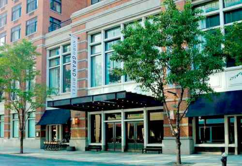 Exterior view of a hotel with large windows, a marquee entrance, and trees lining the sidewalk.