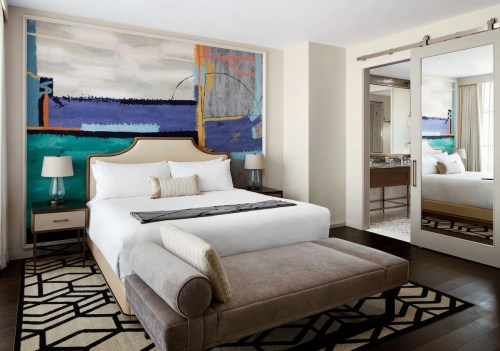 A modern hotel room featuring a large bed, abstract wall art, and stylish decor with a cozy seating area.