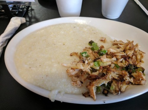 A plate of creamy grits served with seasoned shredded chicken and green peppers on the side.