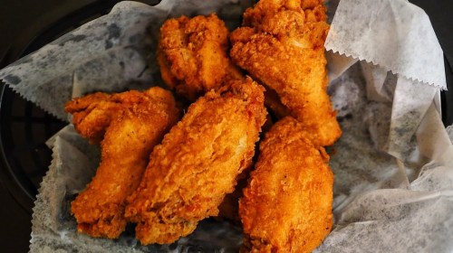A basket of crispy, golden-brown fried chicken wings on parchment paper.