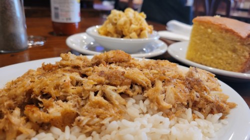 A plate of shredded chicken over rice, with macaroni and cheese and cornbread in the background.