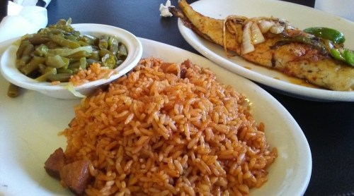 A plate featuring seasoned rice, green beans, and a grilled fish fillet topped with onions and peppers.