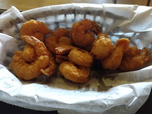 A basket of golden, crispy fried shrimp on a paper-lined tray.