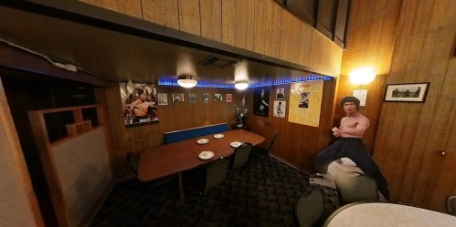 A cozy dining room with wooden walls, a large table, and posters, featuring a life-sized figure of a muscular man.