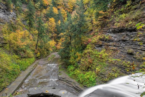 A scenic view of a waterfall cascading down rocky terrain, surrounded by vibrant autumn foliage and lush greenery.