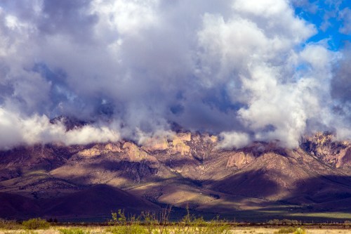 Dramatic mountain landscape with clouds rolling over peaks and shadows across the valley below.