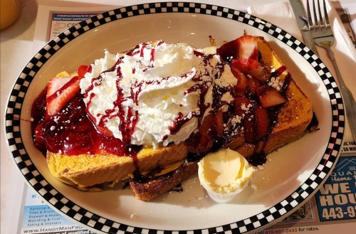 A plate of French toast topped with whipped cream, strawberries, and berry sauce, served with a pat of butter.