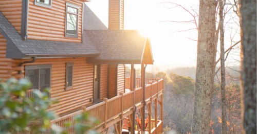 The sun rises over the mountain peak, with a view of a beautiful modern cabin in the foreground.