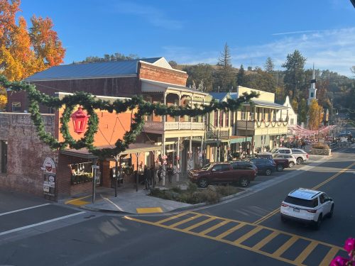 A festive street scene with decorated buildings, people walking, and autumn foliage under a clear blue sky.