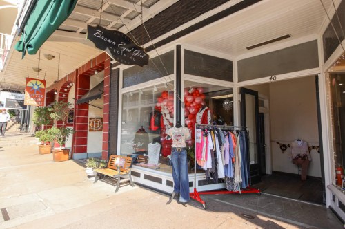 A boutique storefront with clothing displays and balloons, located on a charming street.