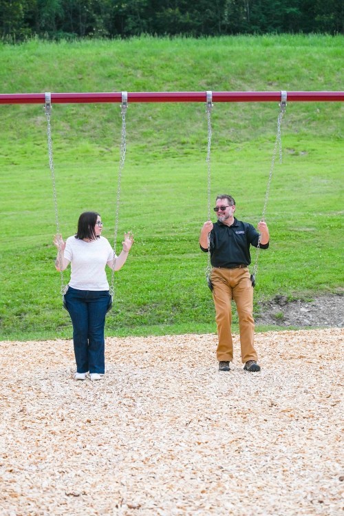 Two people on swings in a playground, smiling and enjoying their time outdoors on a sunny day.