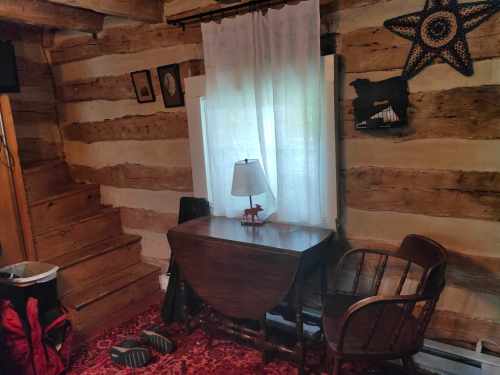 Cozy room with wooden walls, a small desk, chair, lamp, and a window covered by a white curtain.
