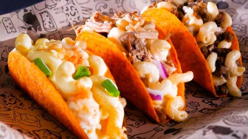Three tacos filled with macaroni and cheese, pulled pork, and ground beef, served in a decorative tray.
