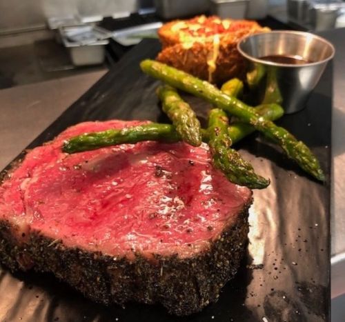 A plate featuring a juicy slice of beef, asparagus, and a small cup of sauce, elegantly presented.