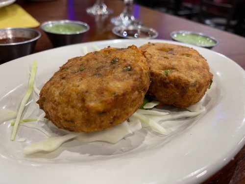 Two golden-brown patties served on a bed of shredded cabbage, accompanied by small bowls of green sauces.