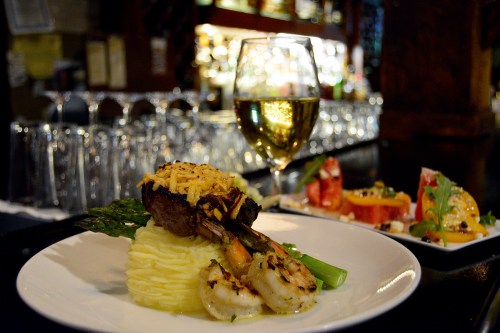 A gourmet dish featuring grilled shrimp, mashed potatoes, and asparagus, accompanied by a glass of white wine.