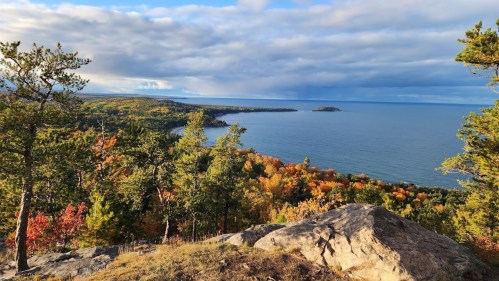 A scenic view of a lake surrounded by colorful autumn trees under a partly cloudy sky.