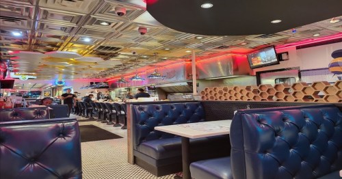 A vibrant diner interior with blue booths, a shiny ceiling, and a bustling kitchen in the background.