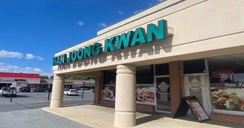 Exterior of Han Joong Kwan restaurant, featuring large green signage and a clear blue sky in the background.