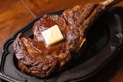 A juicy, grilled tomahawk steak topped with a pat of butter on a sizzling platter.