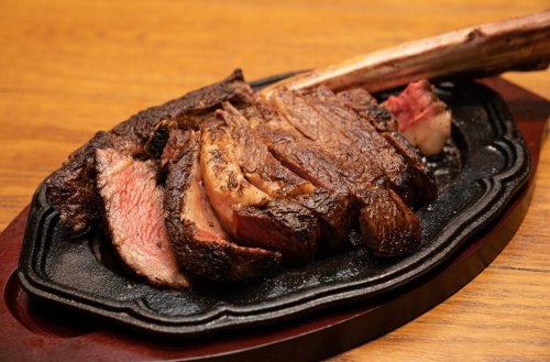 A beautifully cooked, sliced ribeye steak on a sizzling platter, showcasing juicy pink and charred edges.