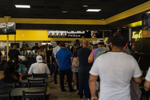 A busy restaurant interior with a long line of customers waiting to order at the counter.