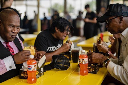 A group of people enjoying burgers and drinks at a vibrant outdoor dining area with yellow tables.