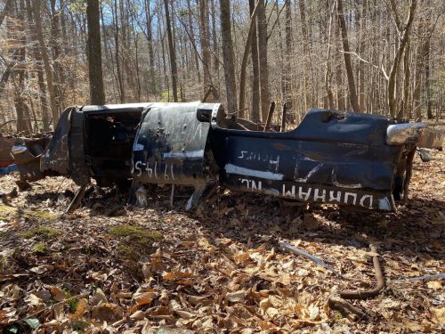 A partially buried aircraft fuselage in a wooded area, surrounded by fallen leaves and trees.