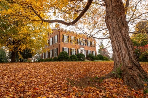 A brick house surrounded by vibrant autumn leaves and trees, showcasing a picturesque fall landscape.