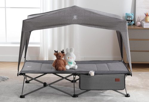 A gray folding cot with a canopy, featuring two stuffed animals sitting on it, in a bright room.