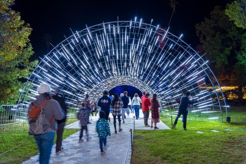 A group of people walks through a glowing, arch-shaped light installation at night.