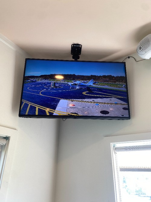 A mounted TV displays a view of an airport runway with planes and taxiways in the background.