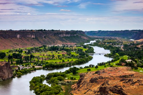 A scenic view of a winding river surrounded by green fields and cliffs under a cloudy sky.