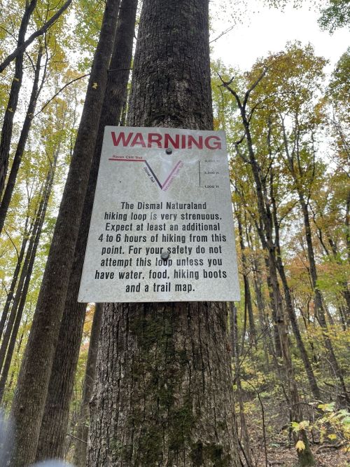 A warning sign on a tree about the strenuous Dismal Naturaland hiking loop, advising hikers to prepare adequately.