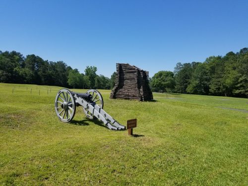 A historic cannon on a grassy field with a wooden structure in the background under a clear blue sky.