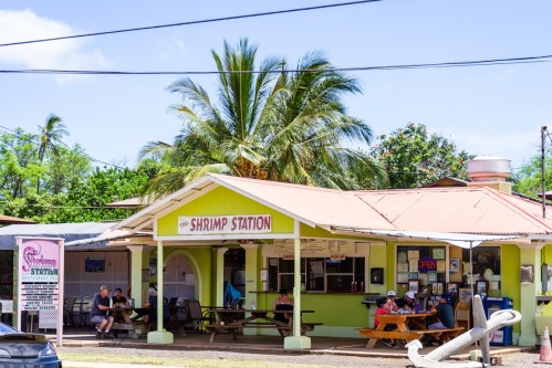 A colorful restaurant called "Shrimp Station" with outdoor seating and palm trees in a sunny setting.