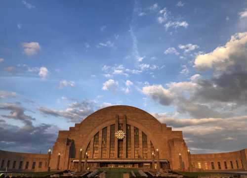 Historic train station with a large clock, set against a dramatic sky with clouds.
