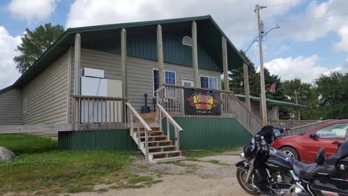 A large, two-story building with a wooden deck, stairs, and a motorcycle parked in front. A sign is visible on the wall.
