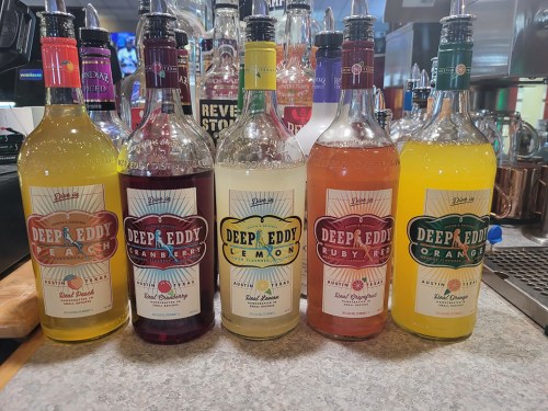 Five bottles of Deep Eddy flavored vodkas in various colors: peach, cranberry, lemon, ruby red grapefruit, and orange.