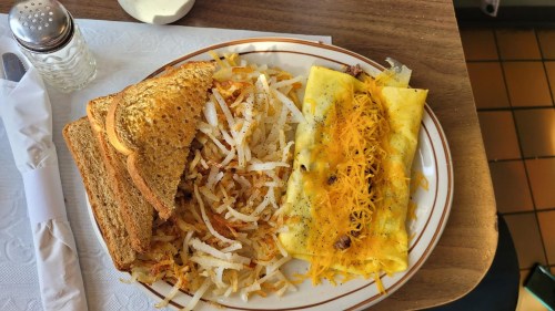 A plate of breakfast featuring two cheese omelets, hash browns, and toast on a wooden table.