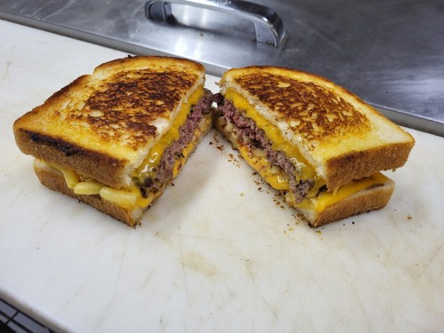 A grilled cheese sandwich cut in half, revealing layers of melted cheese and a juicy beef patty inside.