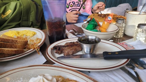 A table set with breakfast items: eggs, toast, hash browns, a drink, and a plate with steak and sauce.