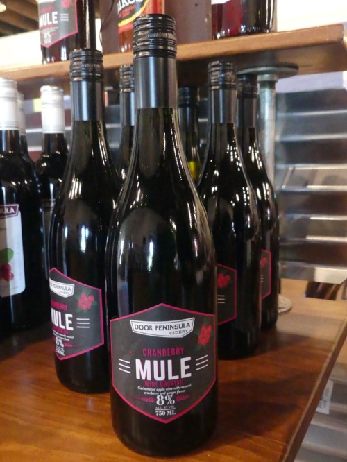 A shelf displaying several bottles of Door Peninsula Cranberry Mule, featuring a black label with red accents.