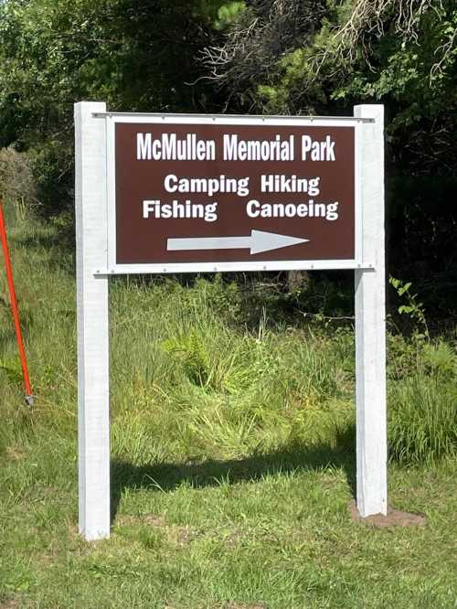 Sign for McMullen Memorial Park with directions for camping, hiking, fishing, and canoeing, pointing left.