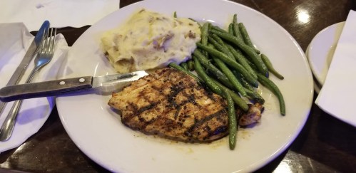 Grilled chicken breast with green beans and mashed potatoes on a white plate. Fork and knife beside the plate.