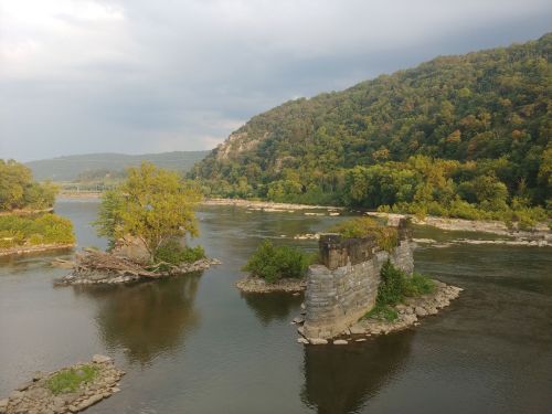A serene river scene with rocky islands and lush greenery, framed by a distant forested hill under a cloudy sky.