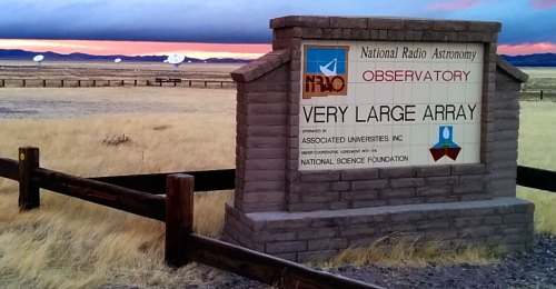 Sign for the Very Large Array Observatory, with a scenic landscape and radio dishes in the background.